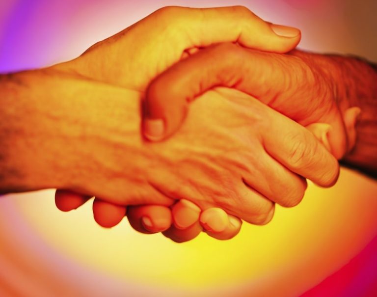 Signatur erfolgreich Zwei Hände schütteln sich vor einem bunten, weich verschwommenen Hintergrund.